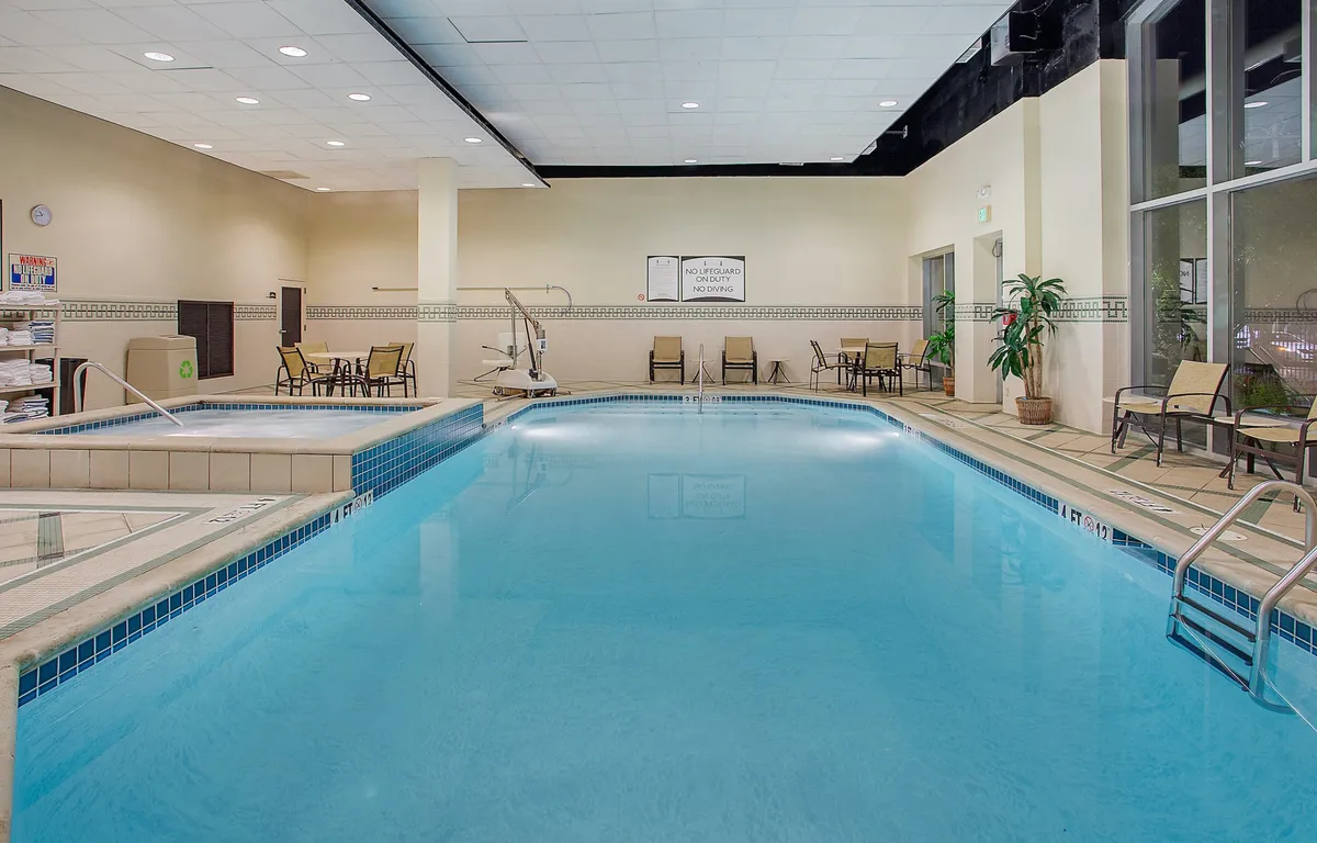 A tranquil interior pool scene featuring the swimming pool, comfortable lounge chairs, and abundant indoor plants. The view captures the atmosphere of relaxation, with soft lighting and poolside social spaces for guests to unwind.