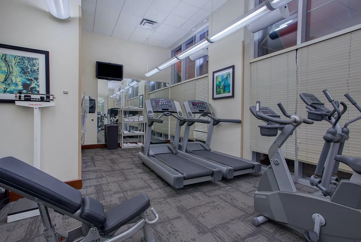 The image showcases a modern fitness center with several treadmills, an elliptical machine, a weight bench, and large mirrors lining the walls. The equipment is neatly arranged, and the space is brightly lit, creating a motivational and energetic atmosphere for guests looking to maintain their workout routines while away from home.
