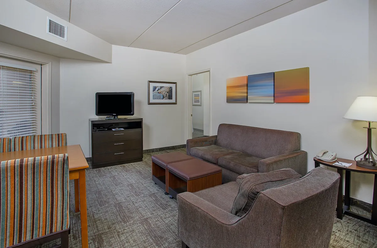 The image showcases a stylish and comfortable living area featuring a plush sofa, a sleek dining table, a large TV, and tasteful wall art. The space is designed for relaxation, socializing, and unwinding after a day exploring downtown Chattanooga.