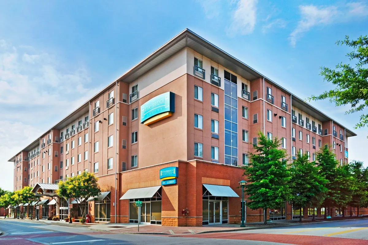 This exterior image captures the building's welcoming facade and the bustling lobby entrance, framed by attractive landscaping and mature trees. Several people are seen gathering outside and approaching the entrance, suggesting a lively, urban environment ideal for business travelers arriving for a conference or exploring nearby attractions.